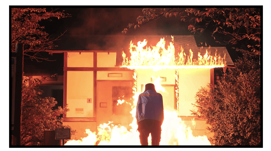 燃え上がる公衆トイレの前に立つ男の姿